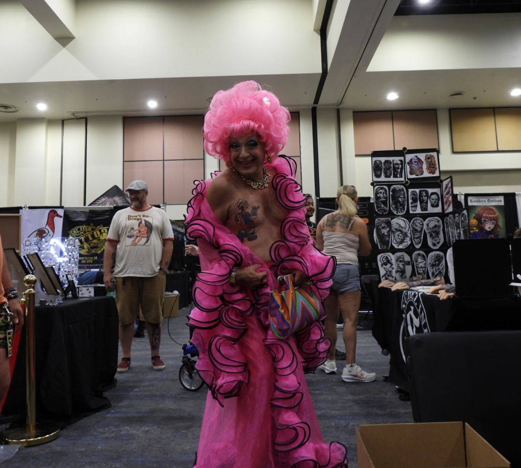 Behind the Booths at Villian Arts Palm Springs 2026 — Convention Life Beyond the Highlight Reel A performer in a bright pink outfit walking through the Villian Arts Palm Springs tattoo convention floor